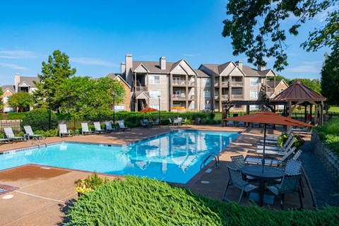 a swimming pool with chairs and umbrellas in front of an apartment building